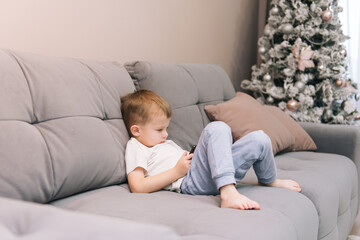 Baby boy sitting on the couch with a phone in his hands, children's dependence on gadgets