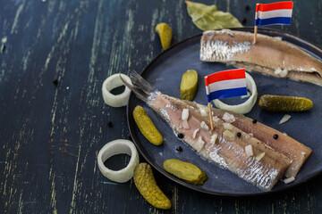 Traditional Dutch food herring fish with pickled cornichons and onion on dark blue ceramic plate...
