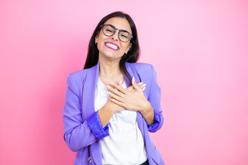 Young business woman wearing purple jacket over pink background smiling with her hands on her chest and grateful gesture on her face.