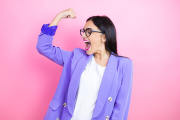 Young business woman wearing purple jacket over pink background showing arms muscles smiling proud