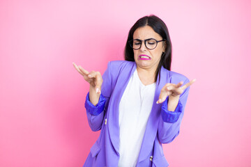 Young business woman wearing purple jacket over pink background disgusted expression, displeased and fearful doing disgust face because aversion reaction. Annoying concept - obrazy, fototapety, plakaty