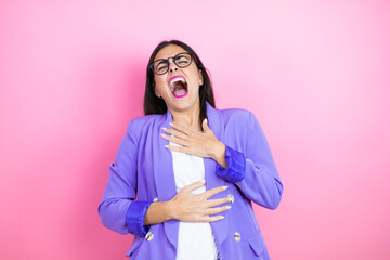 Young business woman wearing purple jacket over pink background laughs happily and has fun keeping hands on stomach.