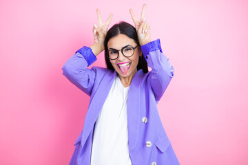 Young business woman wearing purple jacket over pink background Posing funny and crazy with fingers on head as bunny ears, smiling cheerful