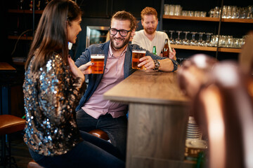Group of cheerful friends standing near bar counter, drinking beer and chatting.