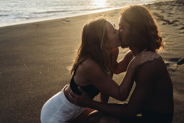 Against the background of sand and ocean in the sun in the sun, a woman in shorts kisses a man. High quality photo
