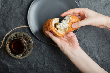 Woman hands holding a fresh croissant on a dark plate