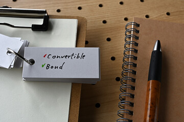 On the desk there is a notebook, a clipboard, and a word book with the word convertible bond.