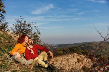 Naklejka na ściany i meble Young happy couple in love enjoying nature. Couple sitting on the ground, hugging and laughing on a beautiful sunny autumn day. It's a weekend.
