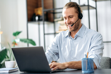 Joyful young adult male manager or call center worker in headset is looks at the laptop screen,...