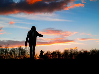 Silhouette of a teenager girl with her small yorkshire terrier in a field against beautiful sunset sky