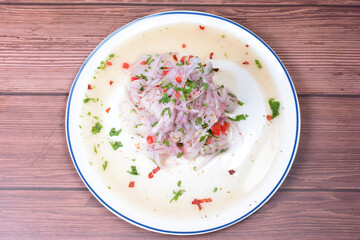 Traditional Peruvian ceviche with fish, onion, lemon, chili peppers, coriander, salt and pepper on wooden background