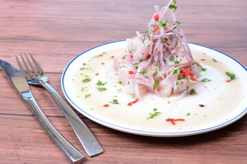 Traditional Peruvian ceviche with fish, onion, lemon, chili peppers, coriander, salt and pepper on wooden background