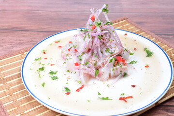 Traditional Peruvian ceviche with fish, onion, lemon, chili peppers, coriander, salt and pepper on wooden background
