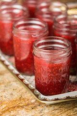 Jars filled with raspberry jam. Filling jars immediately to within half inch of tops prior to putting lids on them. 