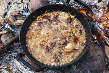 Pieces of lamb with onion are fried in boiling oil on the fire. As a stage in the preparation of traditional pilaf.