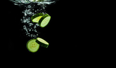 Sliced bio cucumber splashing water isolated on black background.