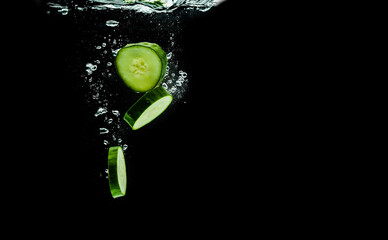 Sliced bio cucumber splashing water isolated on black background.