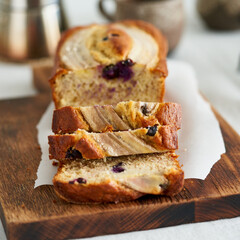 Banana bread, slice of cake with banana and blueberries. Morning breakfast with coffee on light gray linen textile tablecloth on table, Lifestyle still life food. Side view. Close up, macro
