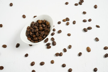 Bodegón minimalista con un cuenco de cerámica lleno de granos de café posado sobre una superficie blanca con textura rústica salpicada de granos esparcidos.