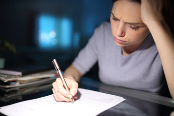 Worried woman filling form in the night at home
