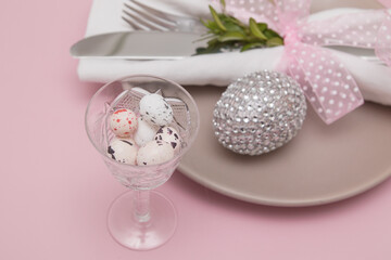 Glass with Easter eggs on the background of plates and cutlery. Variative focus