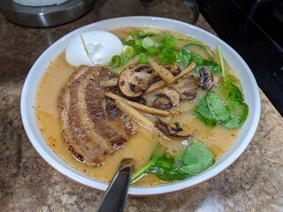 view of homemade pork chashu ramen, served with a soft boiled egg, green onions, mushrooms, and spinach