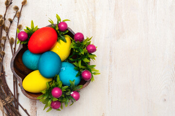 Colorful easter eggs  in wooden plate on white wooden table with branch of willow. Easter backgrounds with copy space for text. Top view. Greeting card. Happy easter concept.