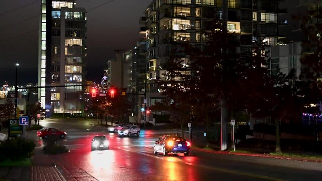 Cars stopping for a red traffic light waiting till it changed to green and proceed there trip over an intersection in downtown Vancouver between skyscrapers. Timelapse by night