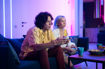Handsome young man teaching how to play the video games to his girlfriend, on the couch, concept about home entertainment, video games.