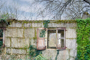 Fototapeta na wymiar Abandoned stone house with broken wooden window. old window with wood in an old Galician house with cloudy sky and vegetation around it.