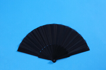 Black hand fan on light blue background, top view