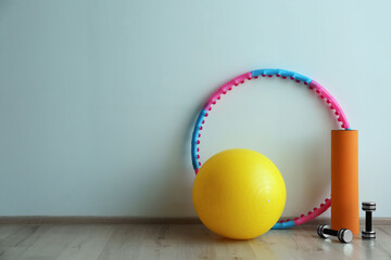 Hula hoop, fitness ball, mat and dumbbells near light wall in gym. Space for text