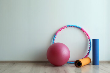 Hula hoop, fitness ball and mats near light wall in gym. Space for text