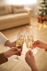 People clinking glasses of champagne in room decorated for Christmas, closeup. Holiday cheer and drink