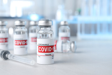 Glass vials with COVID-19 vaccine and syringe on light table. Space for text