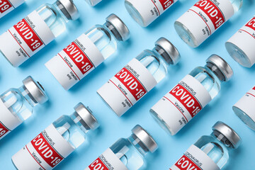 Glass vials with COVID-19 vaccine on light blue background, flat lay