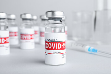 Glass vial with COVID-19 vaccine on light grey table