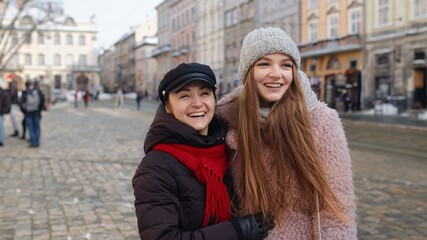 Two smiling women tourists walking together on city street. Family couple talking, having fun, embracing, looking at famous sights of old town. Concept of lesbian LGBT people. Winter holiday traveling