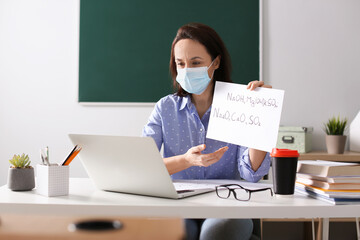 Teacher with protective mask conducting online lesson in classroom during COVID-19 quarantine
