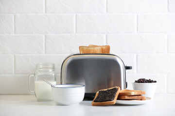 Modern toaster and delicious breakfast on table near brick wall