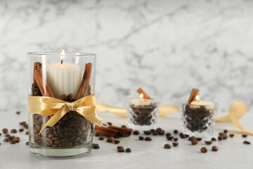 Obraz na płótnie Canvas Glass holders with burning candles, coffee beans and cinnamon on light stone table. Space for text