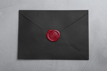 Black envelope with wax seal on grey background, top view