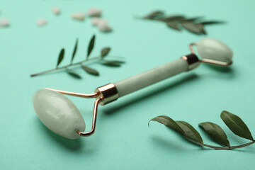 Natural face roller and leaves on turquoise background