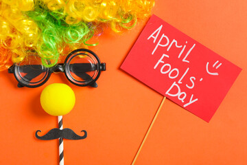 Funny face made of clown's accessories and sign with phrase April Fools' Day on red background,...