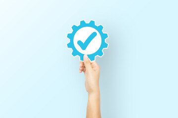 Hand holding paper with icon gear and check mark on light blue background. Concept of Standard...