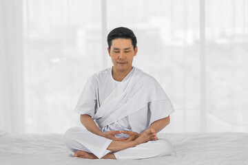 religious asian man wearing white clothing having sitting meditation at home