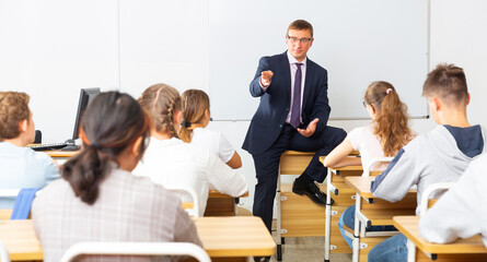 Portrait of professional male teacher giving lesson with interested teenagers in college....