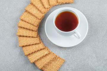 A cup of aroma tea with crackers on a gray background