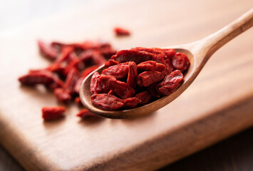 Wolfberries scooped up with a wooden spoon on a wooden background