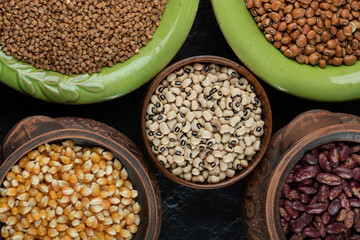 Different kinds of bean seeds, lentil, peas in dishes on a dark background